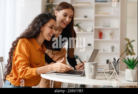 Two Happy Ladies Using Laptop Computer Working Online In Office Stock Photo