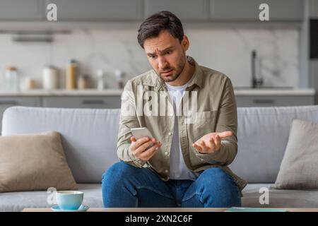 Man Expressing Confusion While Using Phone on Couch at Home Stock Photo