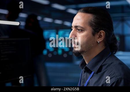 IT developer in data center updating systems to protect servers from exploitable software vulnerabilities. Close up shot of man looking for errors causing equipment to slow down Stock Photo
