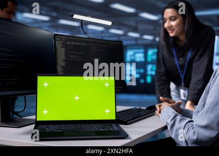 Focus on green screen notebook used by engineers in blurry background to oversee servers used for managing databases. Close up shot of mockup laptop used by IT specialists in data center Stock Photo