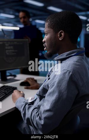 African american engineer in data center updating systems to keeps performance up and protect servers from exploitable software vulnerabilities. Worker looking for errors causing hardware to slow down Stock Photo