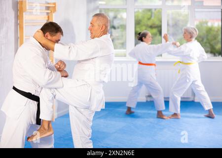 Old man attendee of karate classes fighting with his opponent in sports hall Stock Photo