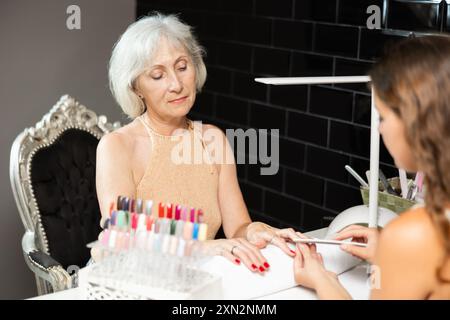 Smiling elderly woman receiving manicure from female manicurist in salon Stock Photo