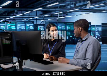 IT staff members using desktop PC to do maintenance in data center to extend equipment life span and avoid downtime. Teamworking colleagues monitoring blade servers for overheating problems Stock Photo