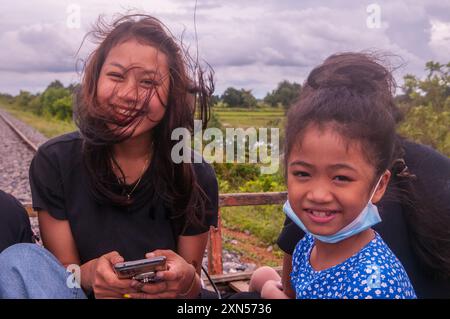 A mixed race woman & a 9 year old Cambodian girl ride the bamboo train during the COVID - 19 pandemic. Battambang Province, Cambodia. © Kraig Lieb Stock Photo