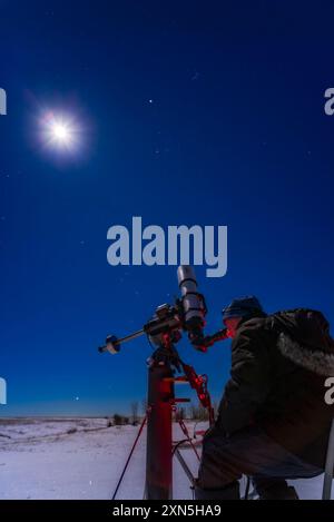 Astronomer observing Mars, the bright reddish star at top on 4 January 2023, with Mars then still bright a month after opposition. The waxing gibbous Moon is the bright object at left. The Pleiades are above Mars; the Hyades and Aldebaran are below Mars. Orion and Sirius are rising in the background below. Photographed from Alberta, Canada. Stock Photo