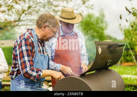 Two senior men enjoying a barbecue in a spring garden. Active retirees cooking together outdoors, demonstrating friendship and social engagement in la Stock Photo