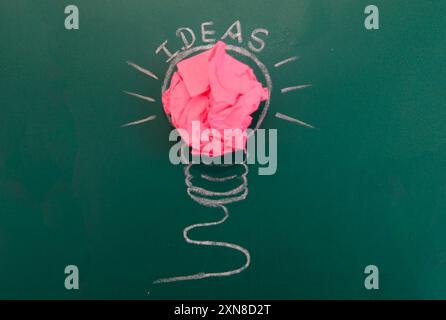 A crumpled pink paper ball sparks creativity within a chalk-drawn light bulb. Stock Photo