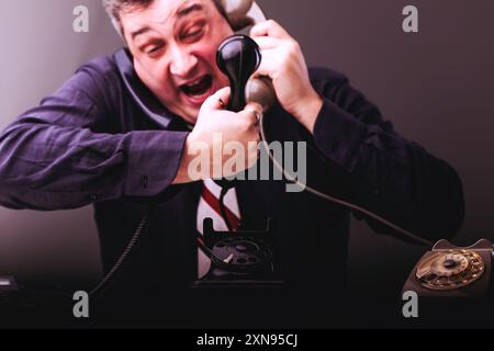 Businessman is experiencing extreme frustration and anger while on a phone call, expressing his emotions by yelling into the receiver Stock Photo