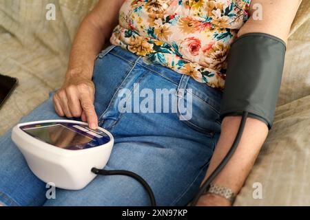 Unrecognizable Senior woman measuring her blood pressure at home. Hispanic Senior Woman Measuring Blood Pressure Using Digital Monitor for Health Stock Photo