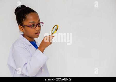 Side view of African American kid wearing white lab coat with magnifier isolated on white background Stock Photo