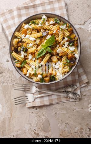 Fusilli pasta with fried eggplant, garlic and feta cheese close-up in a bowl on the table. Vertical top view from above Stock Photo