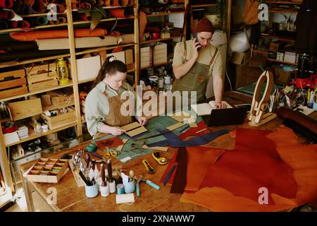 Female tailor with down syndrome cutting out workpieces while her male colleague taking orders via phone Stock Photo