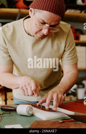 Focused Caucasian tailor cutting leather to create leather wallet in atelier Stock Photo