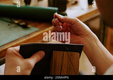 Medium close up of male hands holding leather workpiece and making stitches Stock Photo