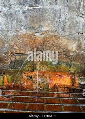 Ancient stone wall with flowing mineral water spring, showcasing historical architecture and nature in harmony Stock Photo