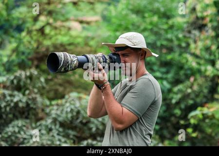 nature photographer, wearing an explorer hat, captures images of wildlife in the jungle using a camera and telephoto lens. highlights the adventure an Stock Photo