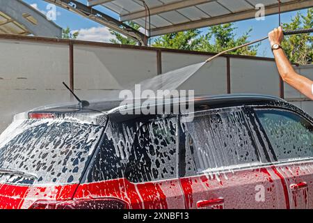 Washing auto with high pressure water jet at outdoor car wash. Stock Photo