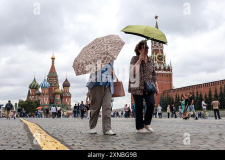 Women with umbrellas walking on the Red Square on background of St. Basil's Cathedral. Rain in city at summer Stock Photo