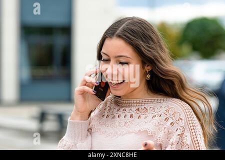 A cheerful young woman engages in a lively phone conversation outdoors. Stock Photo