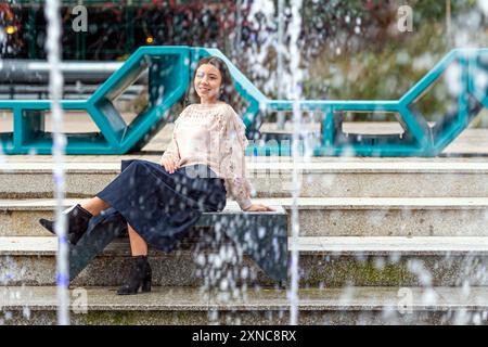 A young woman enjoys a peaceful moment beside a stunning fountain. Stock Photo