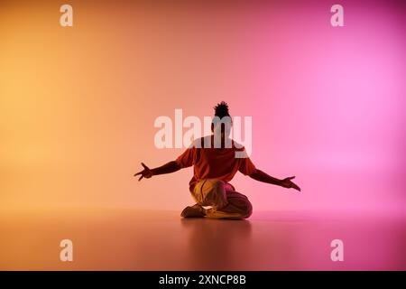 A young African American man dances in front of a gradient pink and orange background. Stock Photo