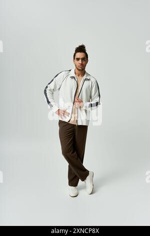 A young African American man, wearing a white tracksuit, poses against a grey background. Stock Photo