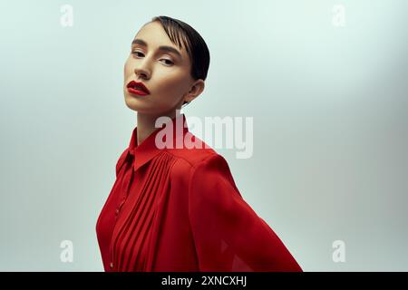 Young woman with short hair in red blouse poses confidently against gray background, creating a striking image. Stock Photo