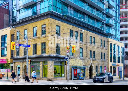 Toronto, Canada - July 30, 2024: People crossing the street by an old brick wall building in the intersection of Sherbourne and King Street East Stock Photo