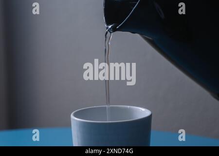 Close-up of hot water pouring into a white tea cup from a black electric kettle on a blue kitchen table Stock Photo