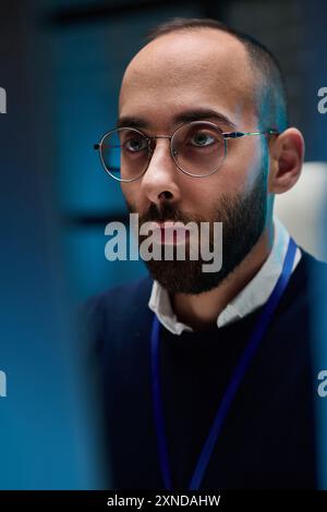 Vertical closeup portrait of adult man looking at computer screen in blue neon light working in cybersecurity Stock Photo