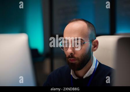 Minimal portrait of bearded computer programmer wearing glasses and looking at screen while working in office with blue light copy space Stock Photo