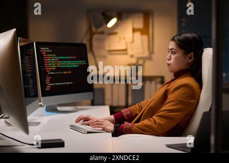 Minimal side view portrait of young woman as female software developer reviewing code working late in office copy space Stock Photo