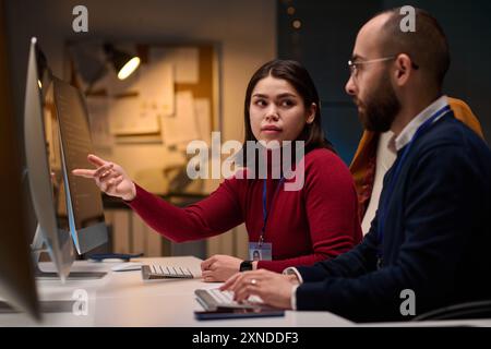 Portrait of computer development team discussing project in office with young woman pointing at screen Stock Photo
