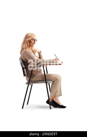 Middle aged woman sitting in a school chair and writing isolated on white background Stock Photo