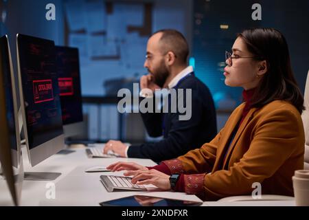 Side view portrait of young woman as female computer programmer working late in cybersecurity department lit by blue light Stock Photo