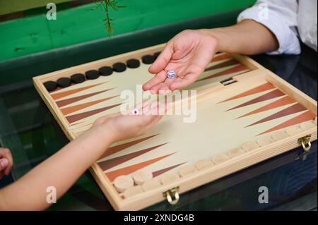 Close-up of two hands shaking dice during a game of backgammon on a wooden board. Perfect for themes of leisure, family time, and traditional board ga Stock Photo