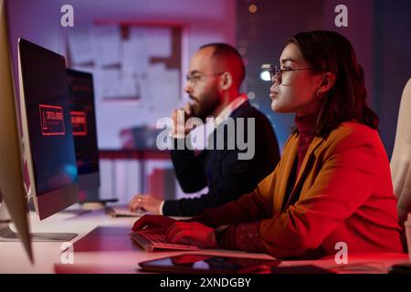 Side view portrait of computer programmers working in cybersecurity department with red emergency lights copy space Stock Photo