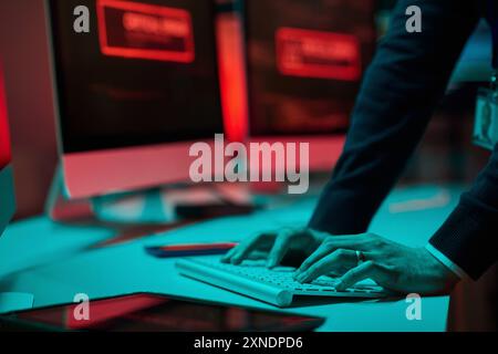 Closeup of unrecognizable man typing on computer keyboard in blue and red light at cybersecurity department copy space Stock Photo
