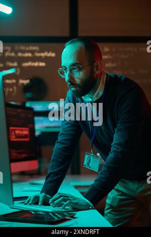 Vertical portrait of bearded cybersecurity engineer working with computer network in blue neon lights Stock Photo