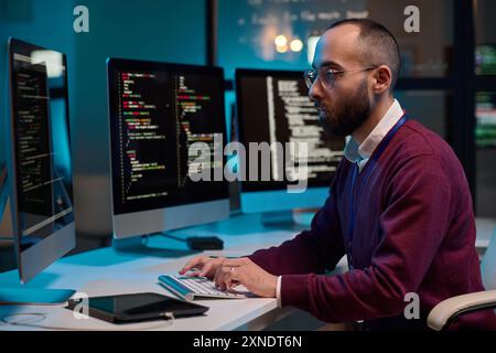 Side view portrait of bearded adult man as cybersecurity engineer typing at computer keyboard while writing code in office copy space Stock Photo