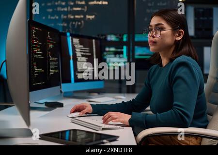 Side view portrait of young woman wearing glasses as cybersecurity engineer typing at computer keyboard and writing code copy space Stock Photo