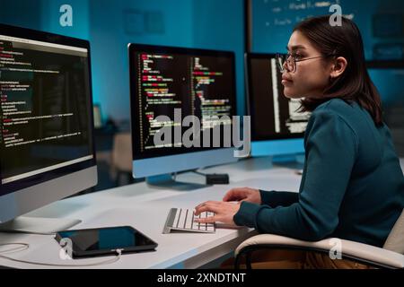 Side view portrait of female computer programmer typing at keyboard and writing code at office workplace copy space Stock Photo