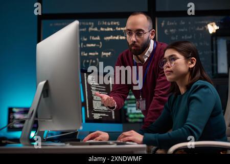 Portrait of bearded adult man as IT development supervisor advising young trainee in office and pointing at computer screen copy space Stock Photo