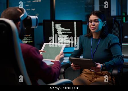 Portrait of young woman wearing glasses and holding tablet developing VR project while working with colleague Stock Photo