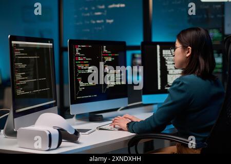 Female IT developer writing code for VR project at office workplace with focus on computer screens copy space Stock Photo