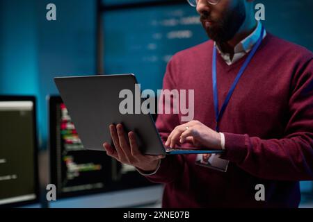 Close up of bearded adult man holding laptop standing in IT development office with blue lights copy space Stock Photo