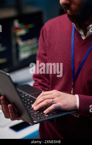 Vertical close up of unrecognizable man holding open laptop standing in IT development office with focus on hand typing Stock Photo