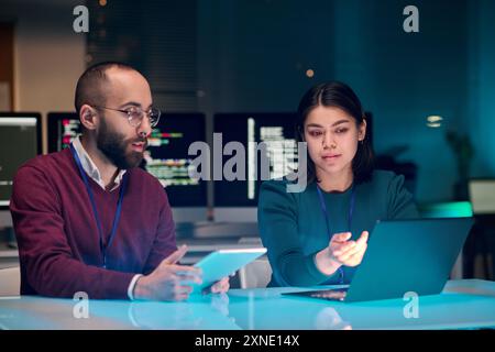 Portrait of young woman as female IT security expert using laptop with male colleague in blue neon light Stock Photo
