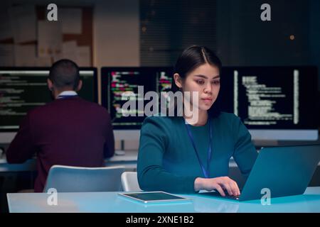 Portrait of young woman as software development expert using laptop at minimal office workplace with blue neon light copy space Stock Photo